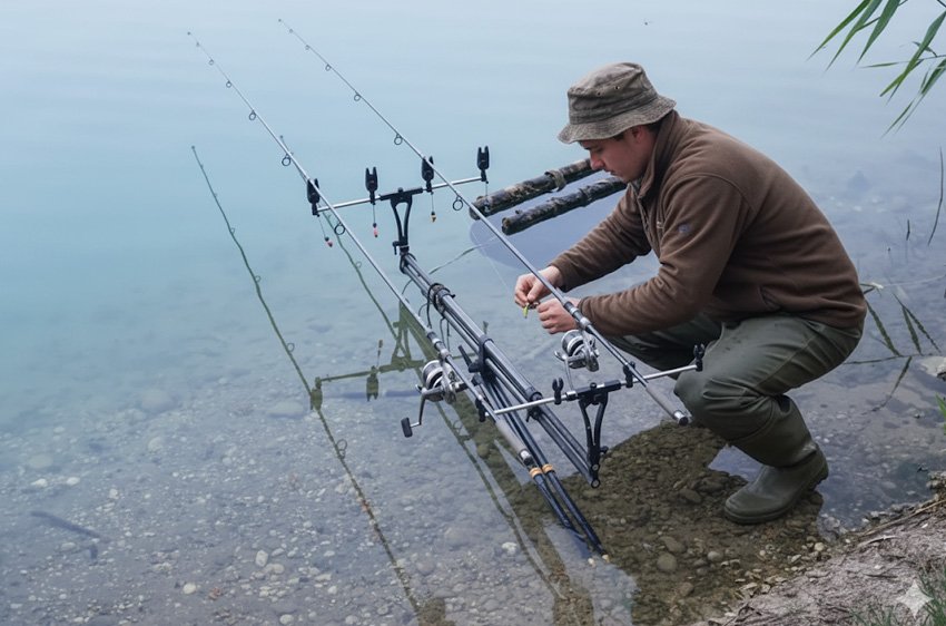 Pescatore che prepara l’attrezzatura su un Rod Pod Morgana Fishing Technology in riva al lago